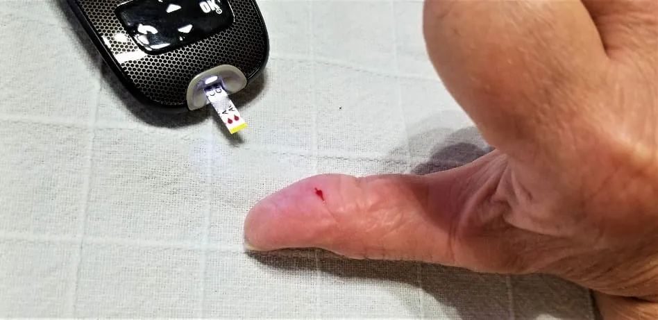 A person testing their blood sugar level with a prick on their thumb and a blood glucose meter.