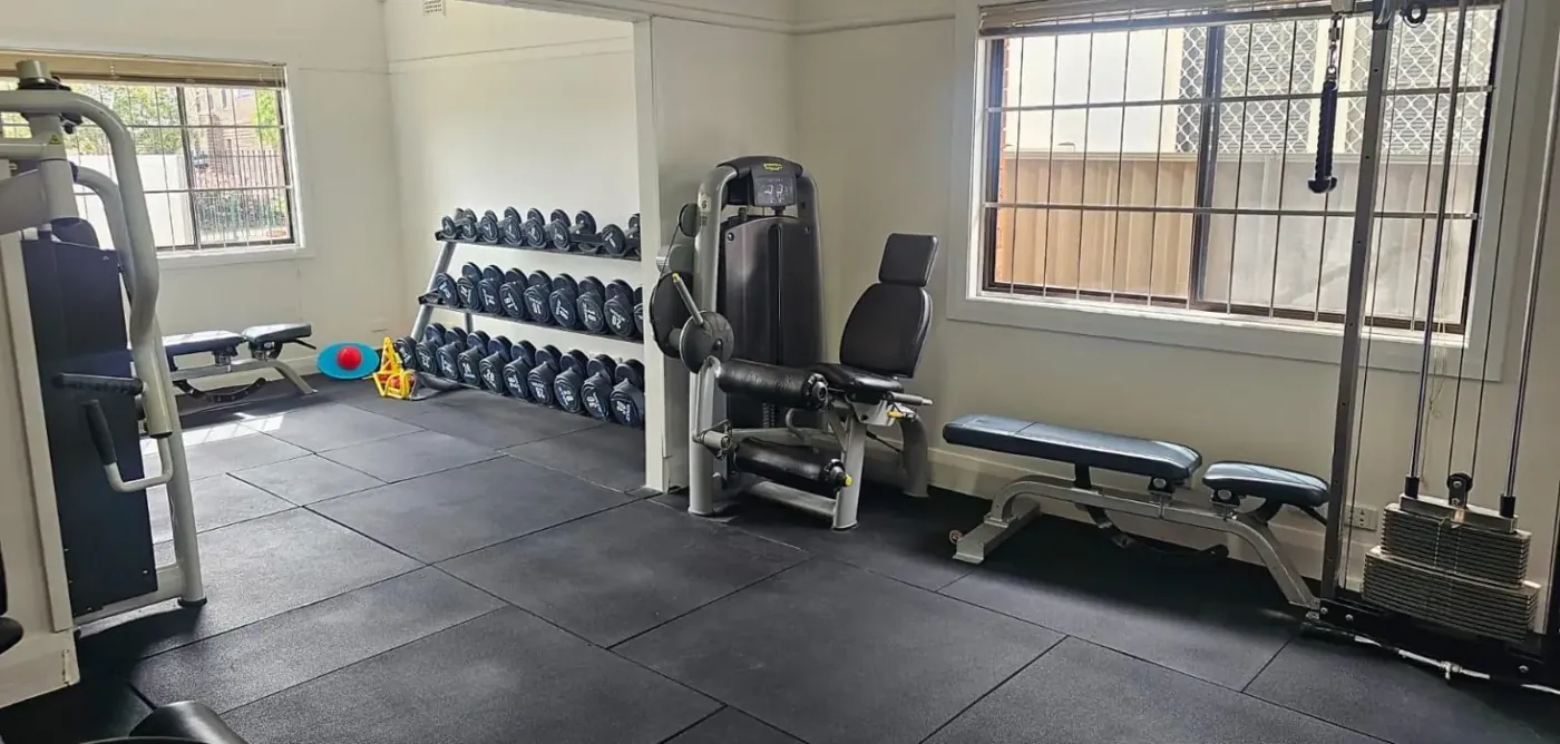 An interior view of an exercise physiology clinic gym with dumbbell racks, weight benches, and resistance training machines.