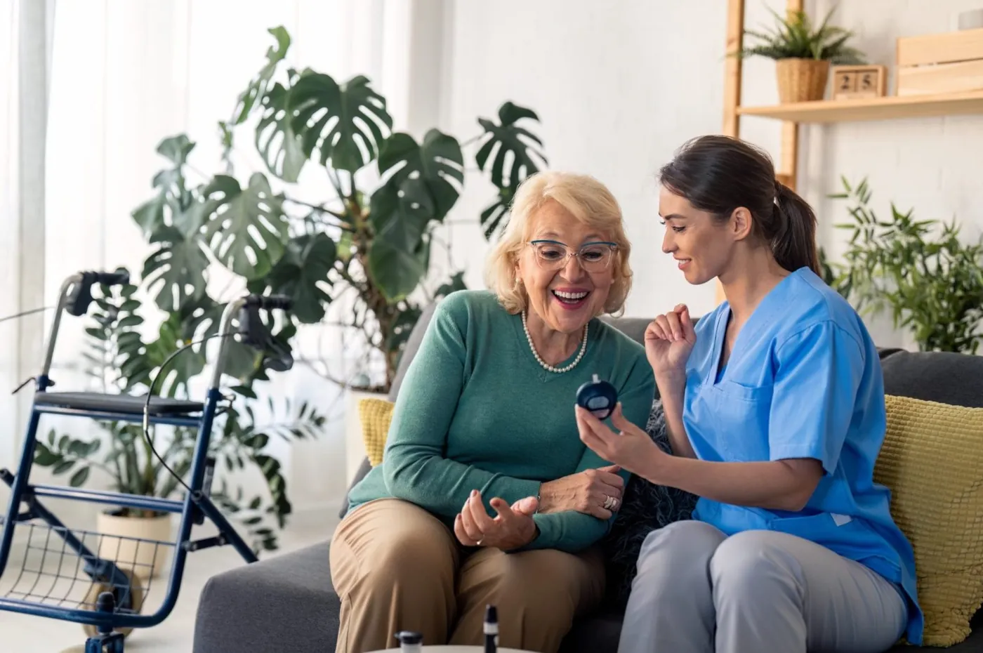 A healthcare practitioner helping an older woman check her blood sugar level on a glucose meter at home.