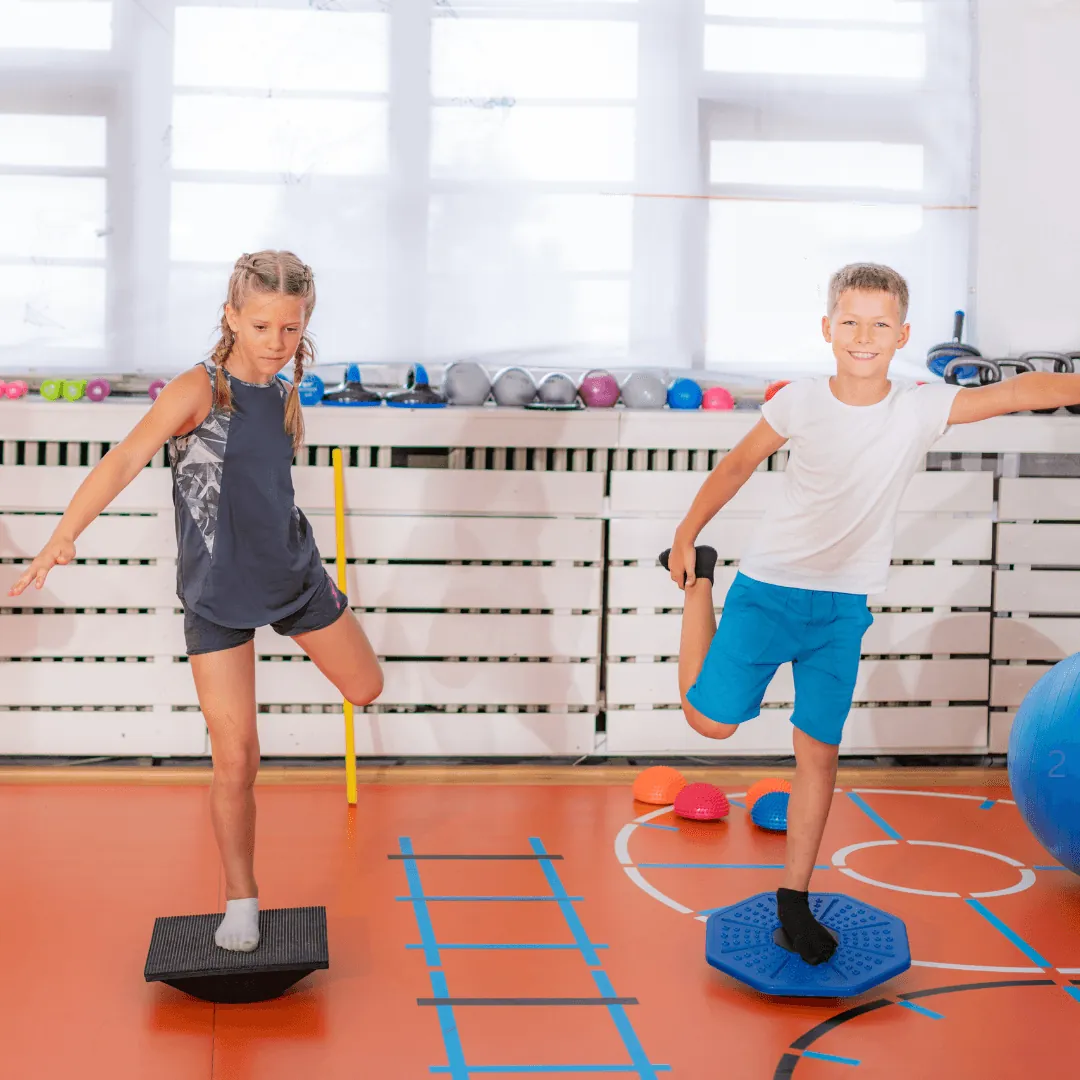 A young boy and girl performing single-leg balance exercises on stability boards during a paediatric exercise physiology session.